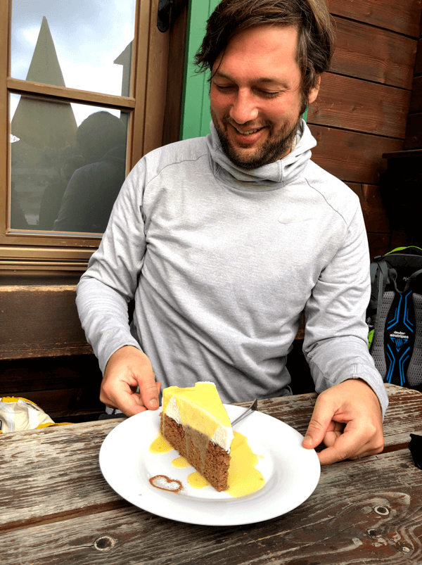 Unser Kollege Bastian freut sich beim Imago Wandertag auf das Stück Kuchen, das vor ihm steht. 